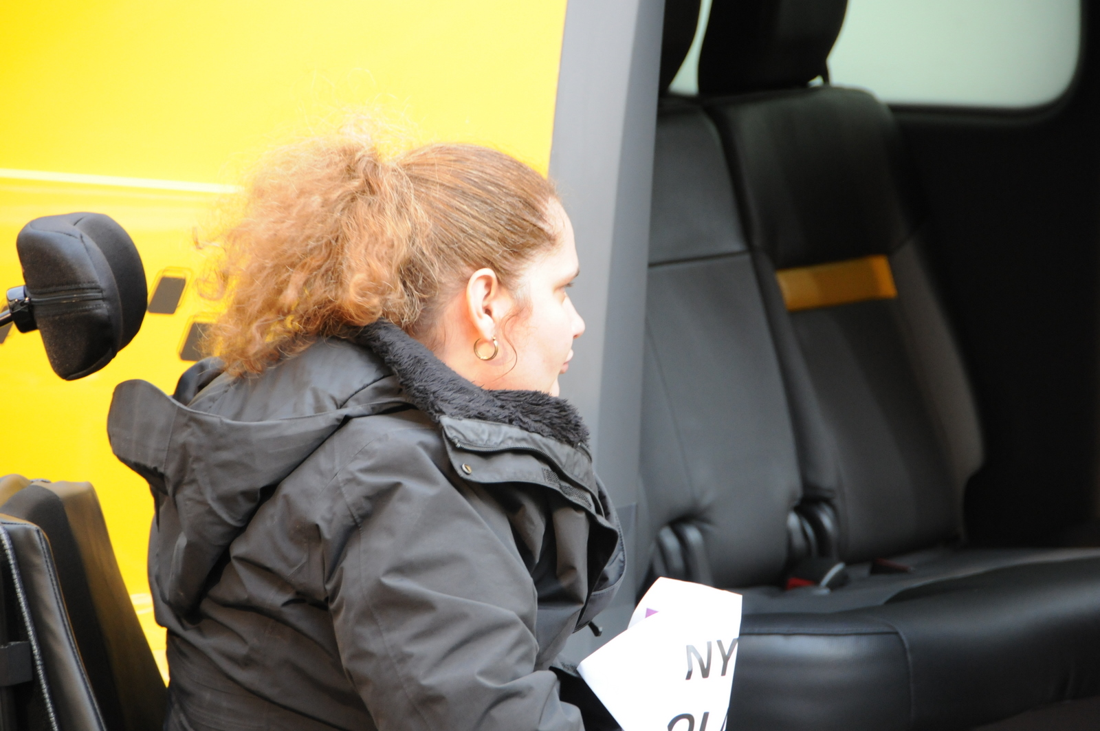 photo of female demonstrator in wheelchair looking at Taxi's inaccessible entrance